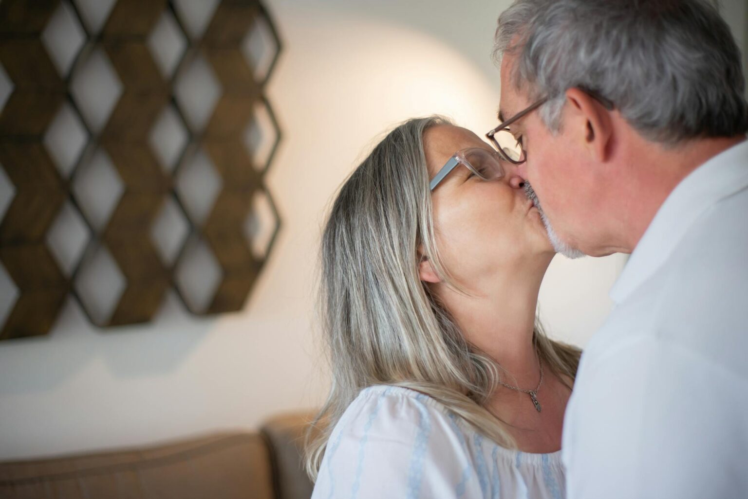 un couple senior échange un baiser tendre dans un salon lumineux, célébrant un amour né grâce à une plateforme de rencontres pour seniors