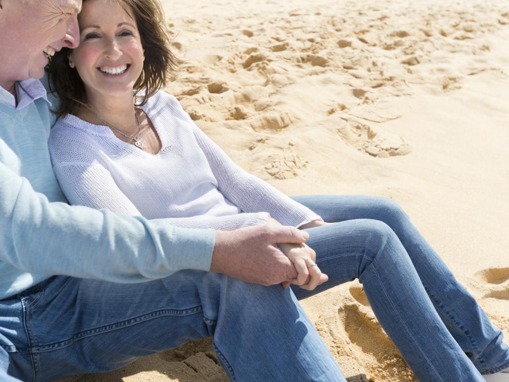 couple mature s'enlaçant tendrement sur la plage, illustrant l'amour et la complicité qui peuvent se développer après 50 ans, dans un cadre paisible et intime