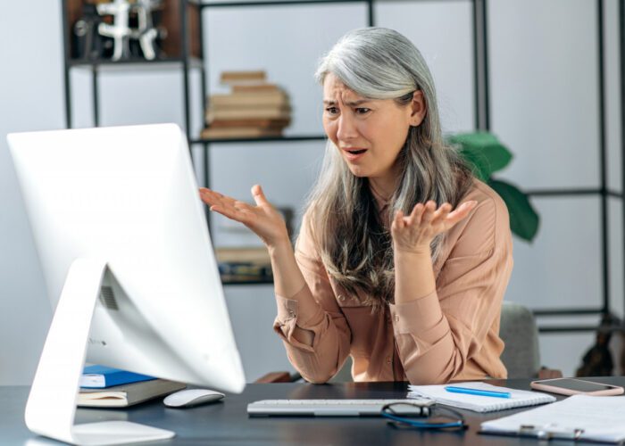 femme visiblement frustrée devant son ordinateur, illustrant les défis de la création d'un profil de rencontre en ligne efficace pour seniors. L’image met en lumière les erreurs courantes à éviter dans la présentation de soi sur les sites de rencontres