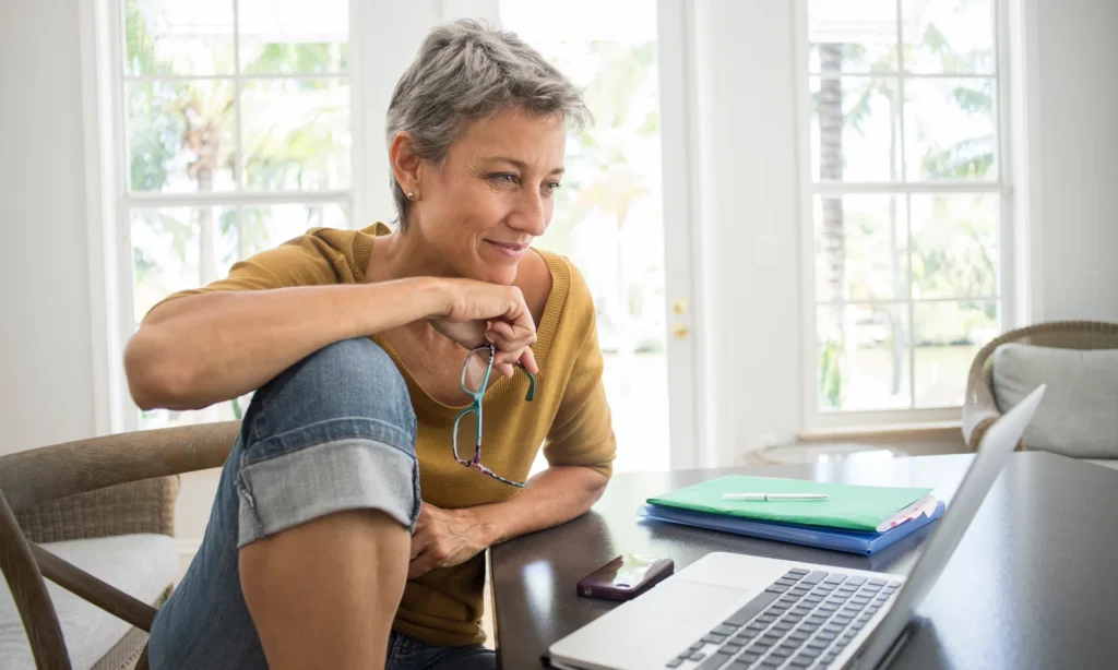 femme senior utilisant son ordinateur avec un sourire, explorant les possibilités de rencontres en ligne pour trouver l'amour, dans un cadre sécurisé et adapté aux célibataires seniors