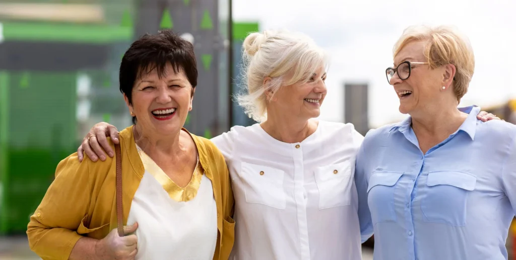 trois femmes seniors souriantes, discutant et profitant d'un moment convivial en extérieur, symbolisant l'importance des sorties amicales seniors pour élargir son cercle social