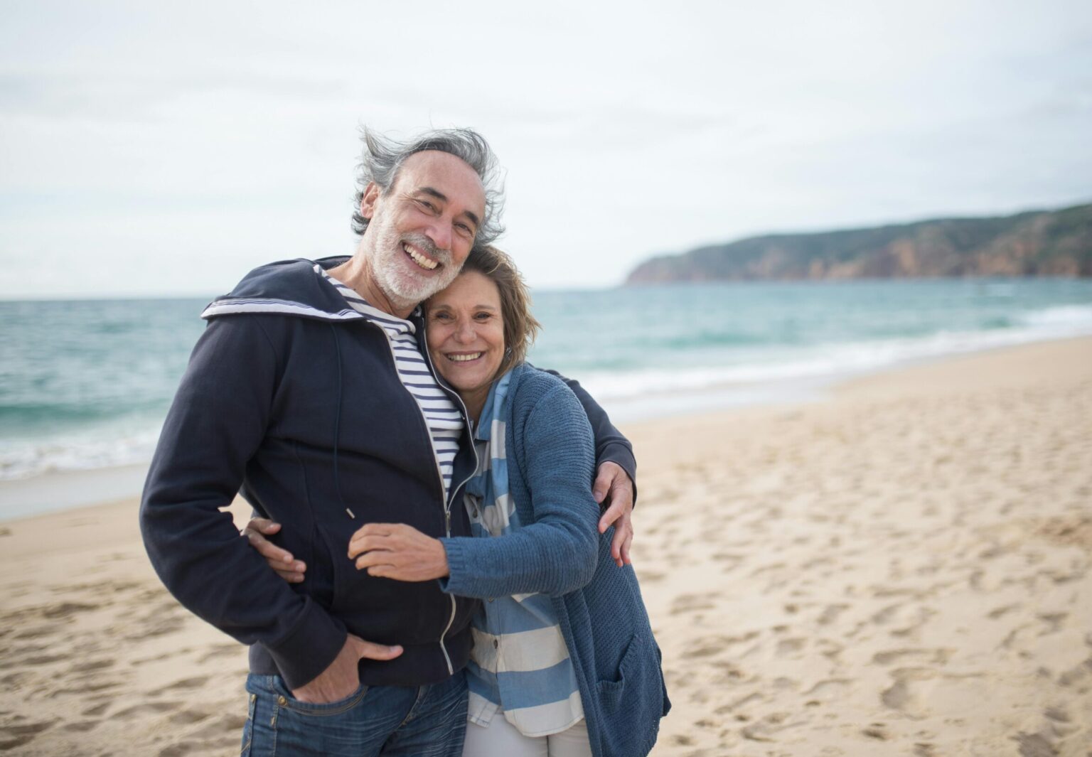 homme et femme seniors profitant d’un moment tendre sur une plage, avec un paysage côtier en arrière-plan