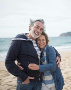 homme et femme seniors profitant d’un moment tendre sur une plage, avec un paysage côtier en arrière-plan