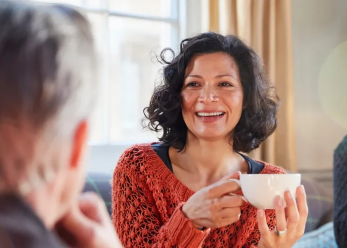 femme souriante partageant un moment convivial avec un groupe d’amis autour d’un café, mettant en valeur l’importance des amitiés et des liens sociaux après 50 ans