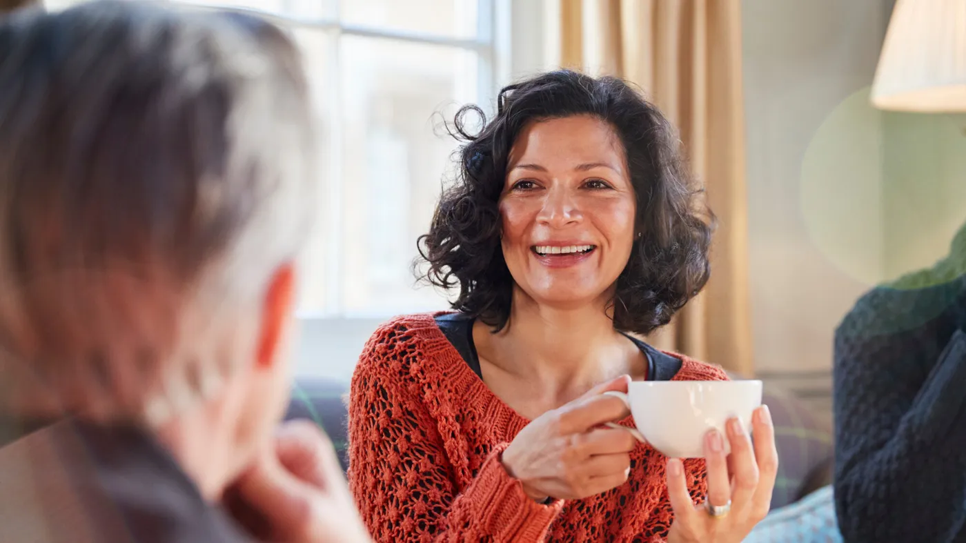 femme souriante partageant un moment convivial avec un groupe d’amis autour d’un café, mettant en valeur l’importance des amitiés et des liens sociaux après 50 ans